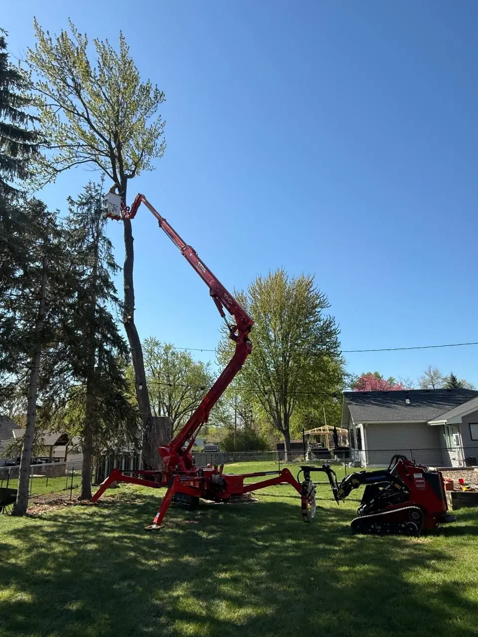CMC Spider Lift with outrigger stabilizers deployed on a residential lawn before tree removal and stump grinding in Minneapolis