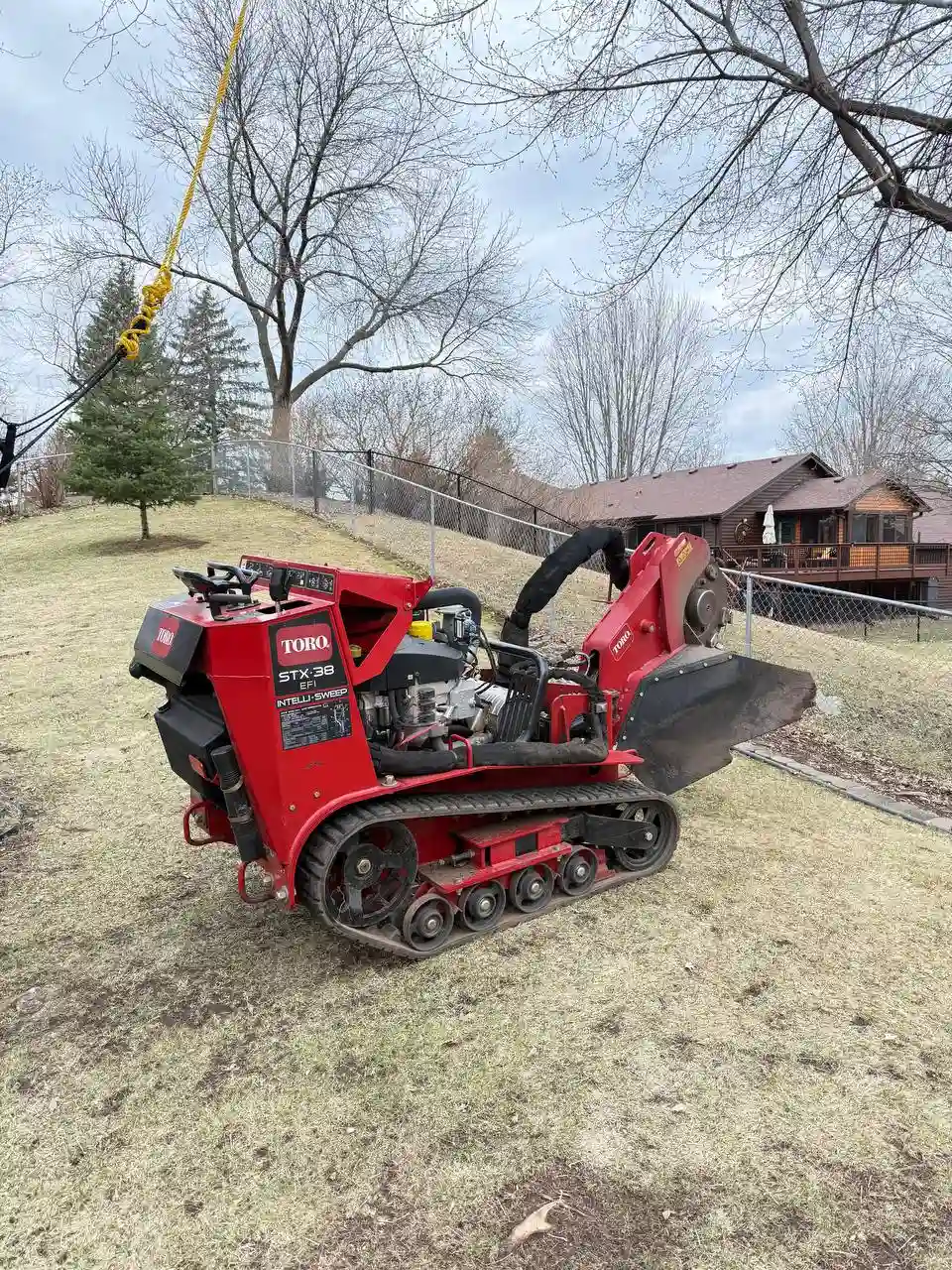 Stump grinder being lowered by crane onto sloped yard in Minnesota