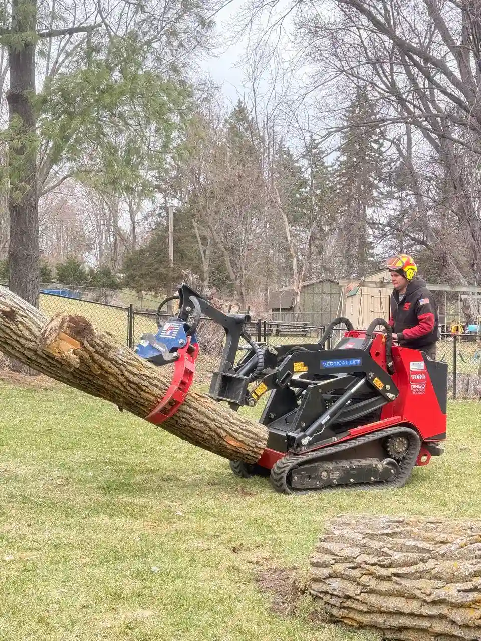 Toro Dingo with grapple lifting a large log during tree removal in Minnesota